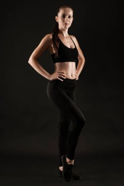 Siyah taytlı esmer kadın, üst ve spor ayakkabılı siyah arka planda poz veriyor. Fitness, spor salonu, sağlıklı yaşam tarzı konsepti. Tam uzunluk.