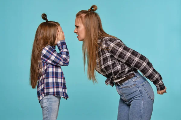 Mãe e filha com penteados engraçados, camisas vestidas com xadrez e jeans jeans jeans azuis estão posando contra um fundo de estúdio azul. Close-up shot. — Fotografia de Stock