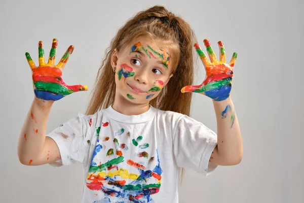 Little girl in white t-shirt is posing standing isolated on white and gesticulating with her painted in different colors palms. Art studio. Close-up. — Stock Photo, Image