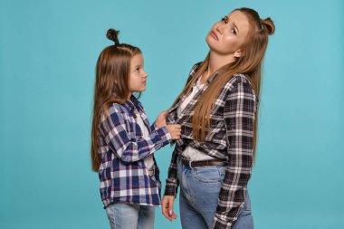 Tuhaf saç stilleri olan, damalı gömlekleri ve kot pantolonu olan anne ve kızı mavi bir stüdyo geçmişine karşı poz veriyorlar. Yakın çekim..