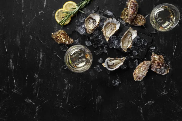 Las ostras frescas, el hielo, el limón en una pizarra rectángulo y el champán están en un fondo texturado de piedra negra. Vista superior con espacio de copia. Cierre. —  Fotos de Stock