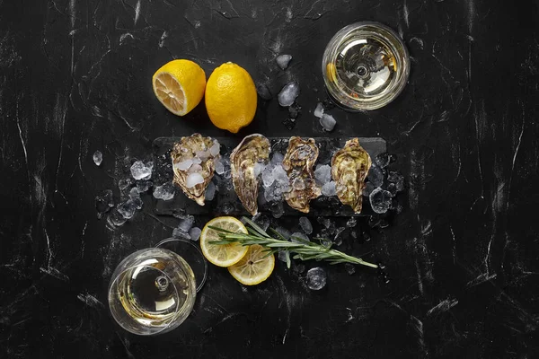 Fresh closed oysters, ice, lemon on a rectangle slate and champagne are on a black stone textured background. Top view with copy space. Close-up. — Stock Photo, Image