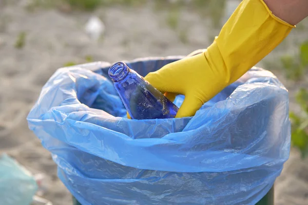 Young volunteer in yellow gloves is walking with garbage bag along a dirty beach of the river and cleaning up trash. People and ecology. Close-up.
