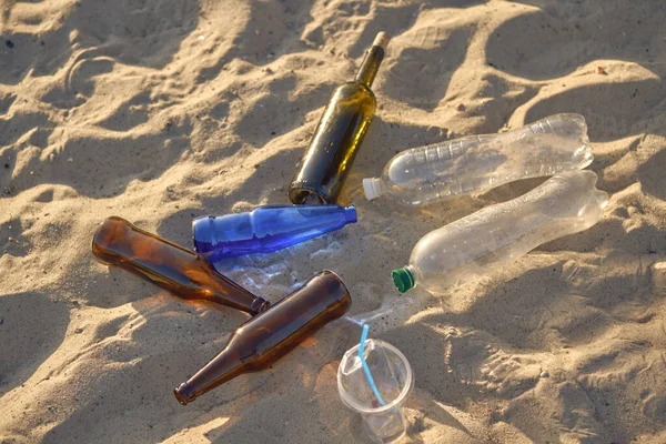 Multi-colored glass bottles, plastic bottles and used cups lies on the sand by the river beach. Cleaning up trash. Volunteering. Close-up, top view.
