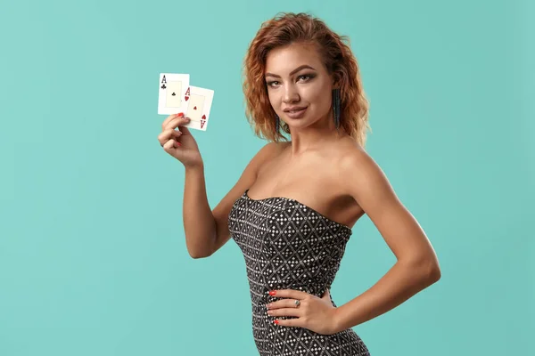 Ginger meisje draagt grijze jurk is poseren met twee speelkaarten in haar handen staande tegen een blauwe studio achtergrond. Casino, poker. Close-up. — Stockfoto