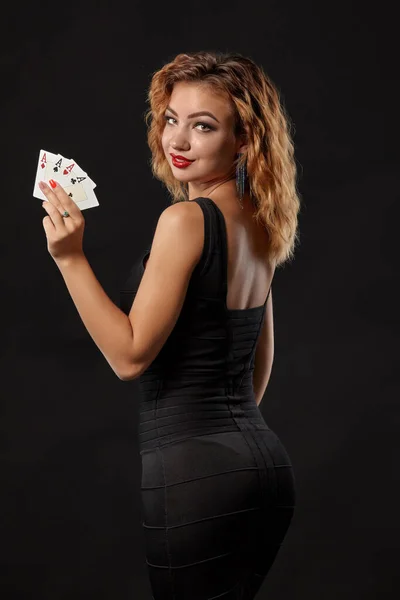Ingefära flicka bär en mörk klänning poserar håller fyra ess i händerna stående mot en svart studio bakgrund. Kasino, poker. Närbild. — Stockfoto