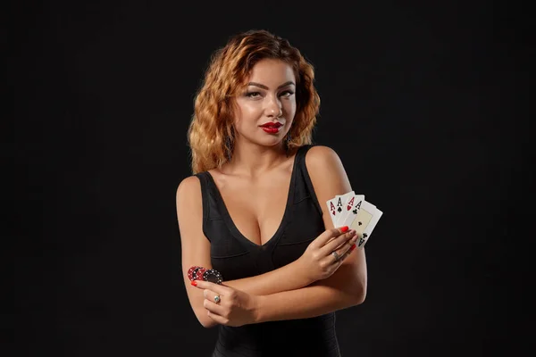 Ginger dívka v tmavých šatech pózuje drží hrací karty a žetony v rukou stojí na černém pozadí studia. Kasino, poker. Detailní záběr. — Stock fotografie
