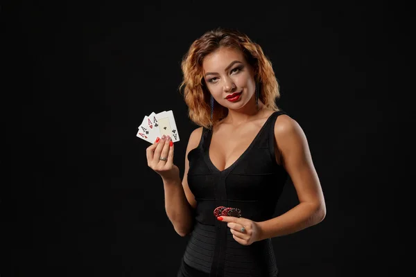 Ragazza zenzero in un abito scuro posa in possesso di carte da gioco e patatine fritte nelle sue mani in piedi su uno sfondo nero studio. Casino ', poker. Primo piano . — Foto Stock