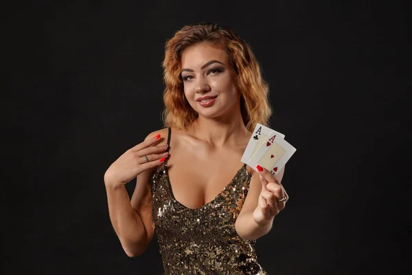 Ginger dívka na sobě lesklé šaty je pózování drží dvě hrací karty v rukou stojí na černém pozadí studia. Kasino, poker. Detailní záběr. — Stock fotografie