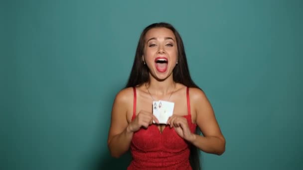 Girl with long hair, wearing in sexy red dress. She is smiling, rejoicing, showing two aces and closing her eyes with them. Blue background. — Stock Video