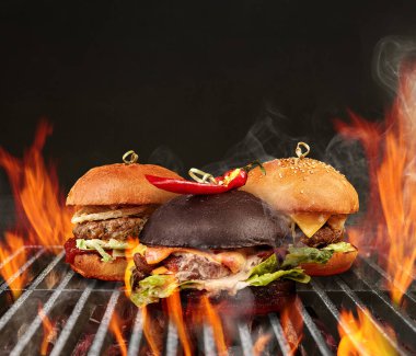 Sığır eti, marul, peynir ve metal portatif barbekü ızgarasında kızartılmış baharatlı kırmızı biberli üç lezzetli hamburger. Kapat.