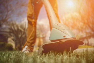 Günlük kıyafetli bir erkek arka bahçesinde elektrikli çim biçme makinesiyle yeşil çimenleri biçiyor. Bahçıvanlık malzemeleri ve hizmetleri. Kapat.