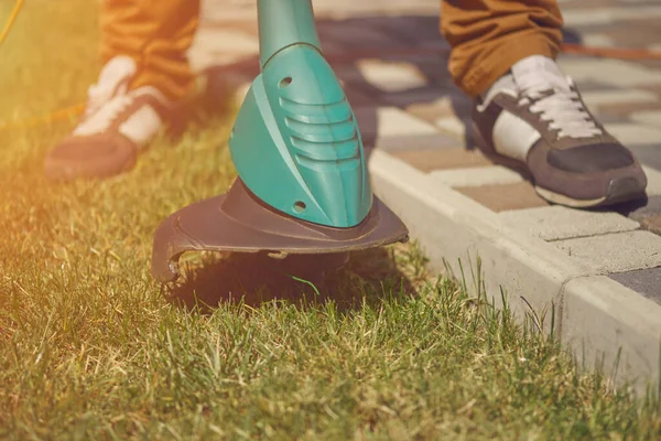 Spor ayakkabılı ve pantolonlu bir erkek bahçesinde el yapımı modern çim biçme makinesiyle yeşil çimenleri kesiyor. Bahçıvanlık ekipmanları ve hizmetleri. Kapat. — Stok fotoğraf