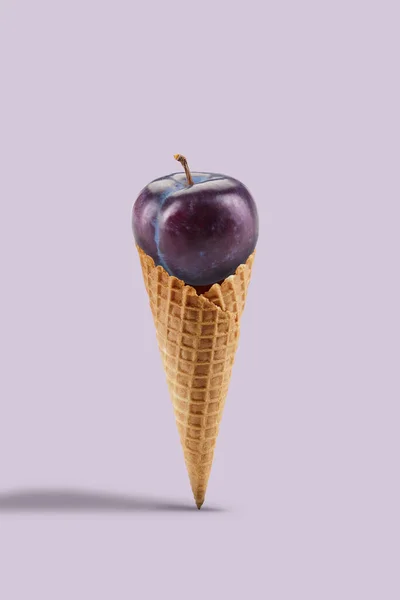 Ciruela púrpura madura en un cono de oblea dulce sobre fondo lila. Nutrición saludable, cosecha estacional de frutas. Cerrar, copiar espacio — Foto de Stock