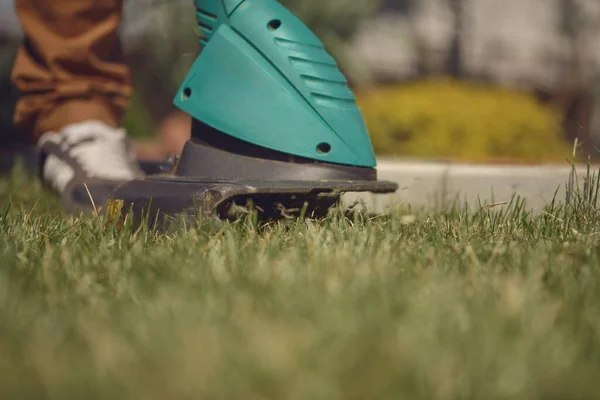Kerl in Turnschuhen und Hose mäht mit professionellem elektrischen Mini-Rasenmäher auf seinem Hinterhof grünes Gras. Gartenpflegegeräte. Nahaufnahme — Stockfoto