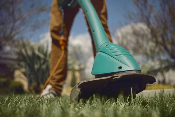Männchen in lässigem Outfit mäht auf seinem Hinterhof grünes Gras mit einem handgeführten Elektro-Rasenmäher. Werkzeuge und Dienstleistungen für die Gartenpflege. Nahaufnahme — Stockfoto