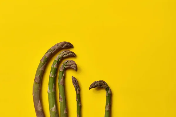 五棵鲜绿色的芦笋生长在黄色的背景上.健康的营养、食物和季节性蔬菜收获。关闭，复制空间 — 图库照片