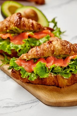 Taze yapılmış kruvasan sandviçleri füme somon, kremalı avokado ve kıtır marul ile dolu lezzetli ve doyurucu bir yemek yaratıyor.