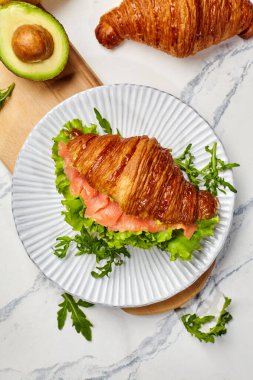 Tütsülenmiş somon, avokado ve yeşilliklerle dolu taze pişmiş kruvasan besleyici bir kahvaltı için tabakta servis edilir.