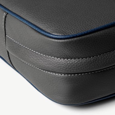 Gri deri çanta köşe detayı beyaz arka plandaki dikişleri ve mavi boruları vurguluyor.