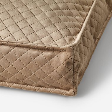 Yumuşak, bej kaplı kadife yastık, dikişlerin ve dikişlerin işçiliğini vurguluyor.