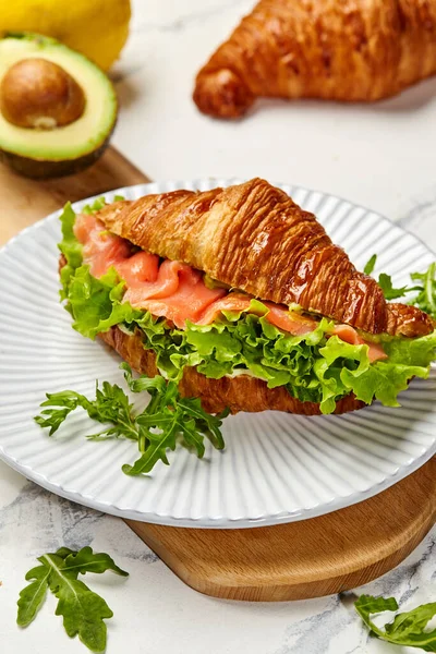 Tütsülenmiş somon, avokado, marul ve roka ile dolu kruvasan sandviçi sağlıklı ve lezzetli bir yemek oluşturur.