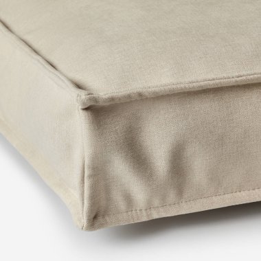Köşedeki dikiş detaylarının altını çizen bej bir kumaş yastığın yakın çekimi.