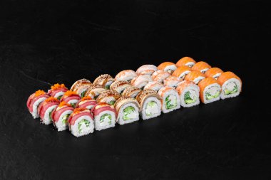 Renkli suşi rulolarının çeşitliliği karanlık bir sayfaya dizilmiş, çekici bir mutfak sahnesi yaratıyor.