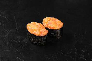 İki parça baharatlı Gunkan maki suşisi, doğranmış somon ve tobiko, parlak, siyah bir arka planda dinleniyor.