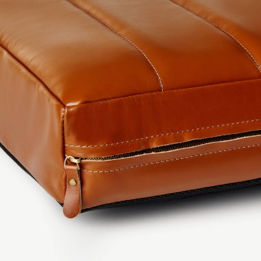 Fermuarlı kahverengi deri yastık, işçiliği ve dikişlerin kalitesini vurguluyor.