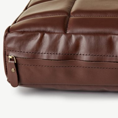 Kahverengi deri bir çantanın yakın çekimi fermuarın kapanmasını ve karmaşık dikişleri vurguluyor, kaliteli işçiliği vurguluyor.