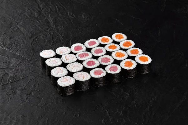 Hosomaki suşi ruloları, siyah desenli bir yüzeye yerleştirilmiş farklı dolgularla görsel olarak çekici bir sunum oluşturur.