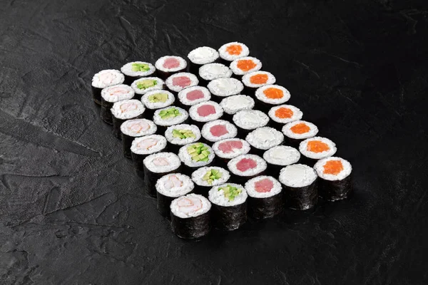 Siyah arka planda dikdörtgen oluşturan renkli Hosomaki lezzetli bir suşi deneyimi için çeşitli dolguları sergiliyor.