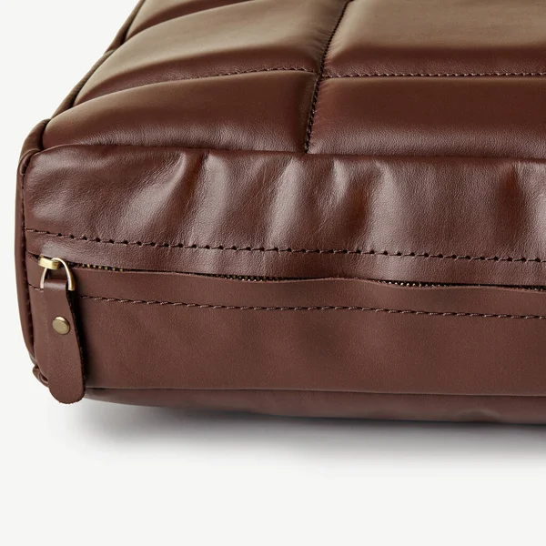 Kahverengi deri bir çantanın yakın çekimi fermuarın kapanmasını ve karmaşık dikişleri vurguluyor, kaliteli işçiliği vurguluyor.