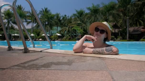 Schönes junges Mädchen mit Brille steht im Pool blickt in die Kamera und korrigiert Handmütze — Stockvideo