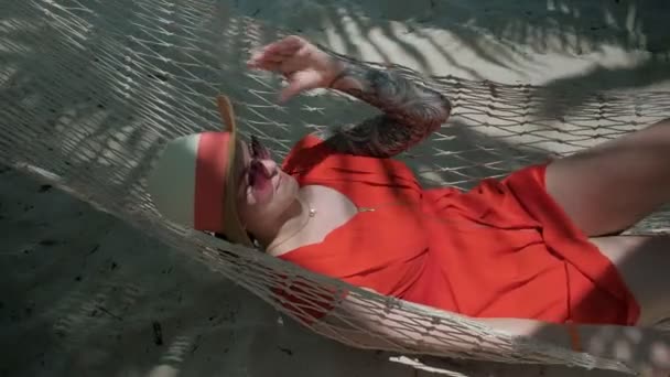 Jonge gelukkige vrouw in rode jurk liggend op de hangmat op het strand zand eiland — Stockvideo