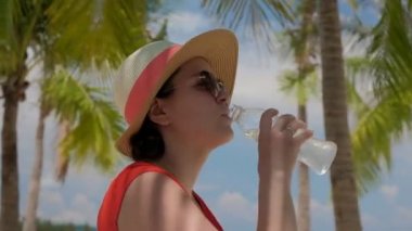 Genç kadın kırmızı elbise ve şapka güneş içme suyu palmiye ağaçları arka plan üzerinde seyir