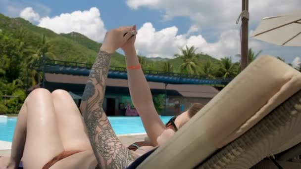 Ung tatuerad kvinna använder sin smartphone och ta bilder av sig själv liggande på en solstol — Stockvideo