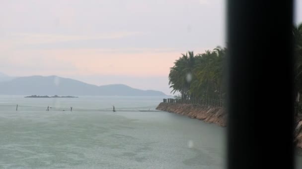 Тропічний дощ біля берега океану з пальмами та горами на задньому плані — стокове відео