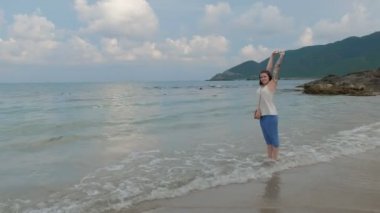 Güzel mutlu birkadın okyanus kıyı tarafından ellerini yukarı kaldırarak ve manzarayı yürüyor