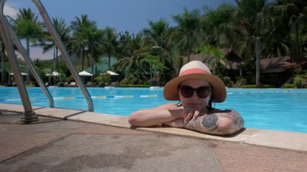 Bela jovem com óculos fica na piscina olha para a câmera e coquete sorrindo — Vídeo de Stock