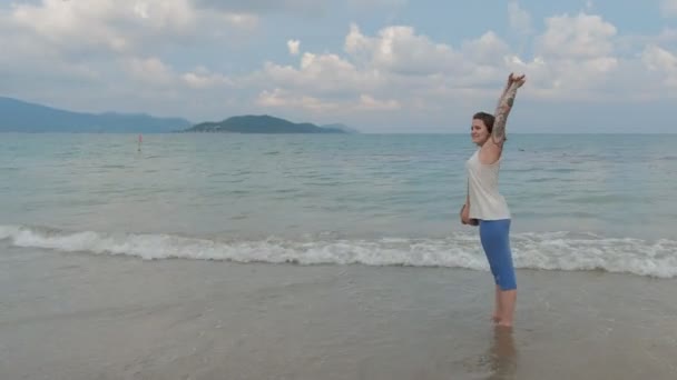 A beautiful tattooed woman is walking by the ocean shore, strerching and enjoying the view — Stock Video