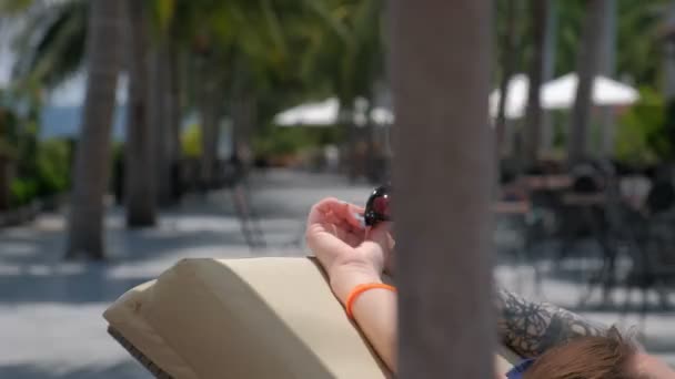 Een close-up van vrouwelijke handen met tinten met palm bomen steegje op de achtergrond — Stockvideo