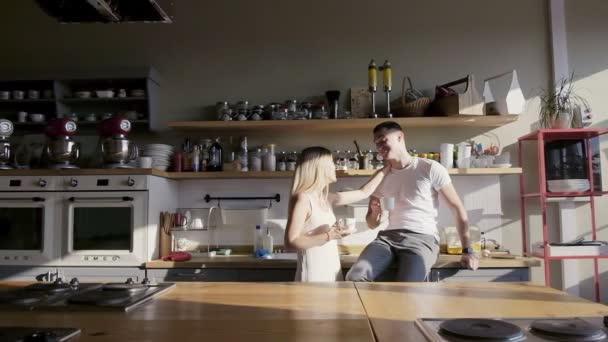 Una pareja feliz está tomando café en la cocina, riendo y sonriendo — Vídeos de Stock