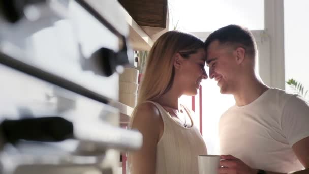 Una pareja feliz y cariñosa está besando, abrazando y bebiendo café en la cocina soleada — Vídeos de Stock