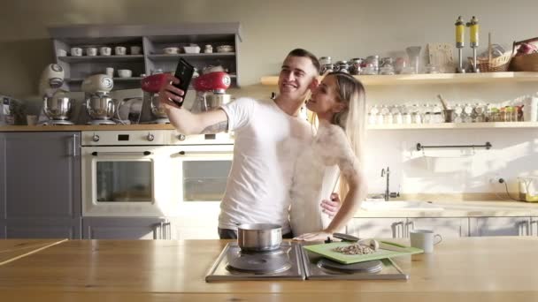 美しいカップルが楽しんで台所で selfies、ハグ、料理を取って晴れた朝 — ストック動画
