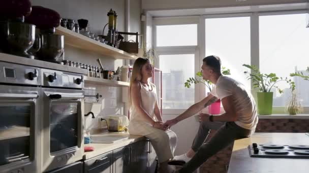 Boldog mosolygó pár enjoyin van a napfényes reggel a konyhában, és közben ül a munkalapok, és beszélt — Stock videók