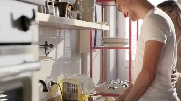 Красивый европейский мужчина готовит и разговаривает со своей красивой улыбчивой женой на кухне — стоковое видео