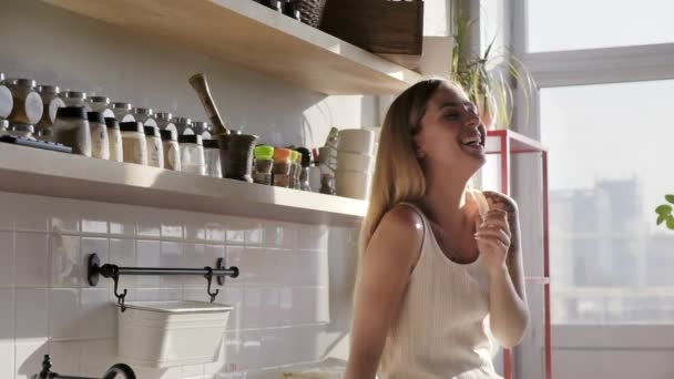 Um close-up de uma bela jovem sorridente está falando e rindo na cozinha ensolarada — Vídeo de Stock