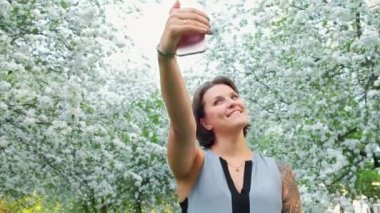 Genç sevimli dövmeli kadın selfie çiçek açan elma bahçesi cep telefonu üzerinde alma